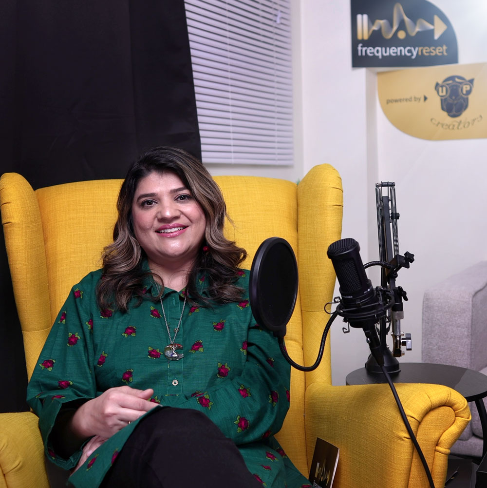 Sobia sits in a yellow chair infront of her podcast mic for Frequency Reset